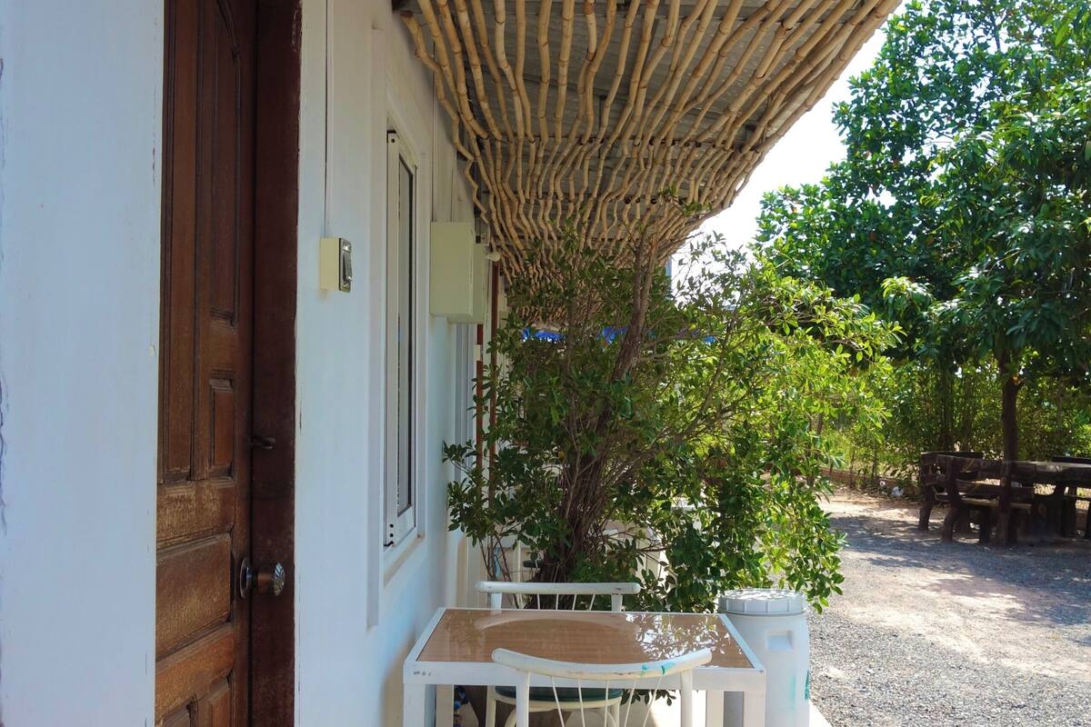 A covered outdoor seating area with a table and chairs, a wooden door, and a sign above the door.