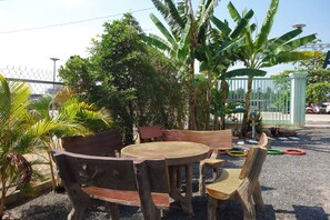 Ein Gartenmöbel-Set aus Holz bestehend aus einer Bank und einem Tisch, mit einem Zaun, Bäumen und einem Gebäude im Hintergrund.