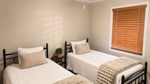 A bedroom with two beds, a ceiling fan, a window with blinds, and a bedside table with a plant.
