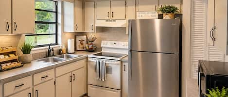 A modern kitchen with stainless steel appliances, a window, and a view of greenery outside.