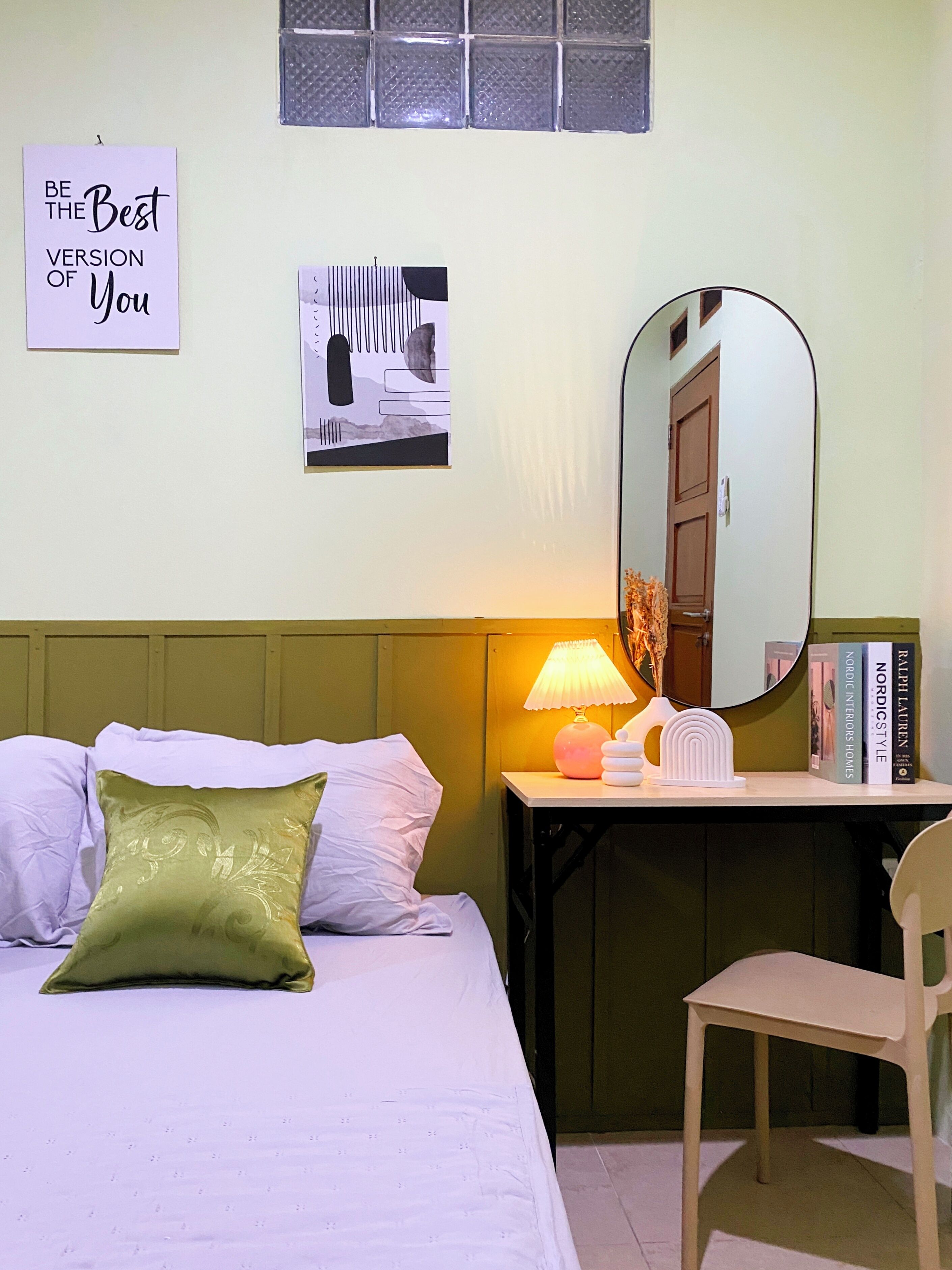A bedroom with a bed, a desk, a chair, a lamp, a mirror, and two books on the wall.