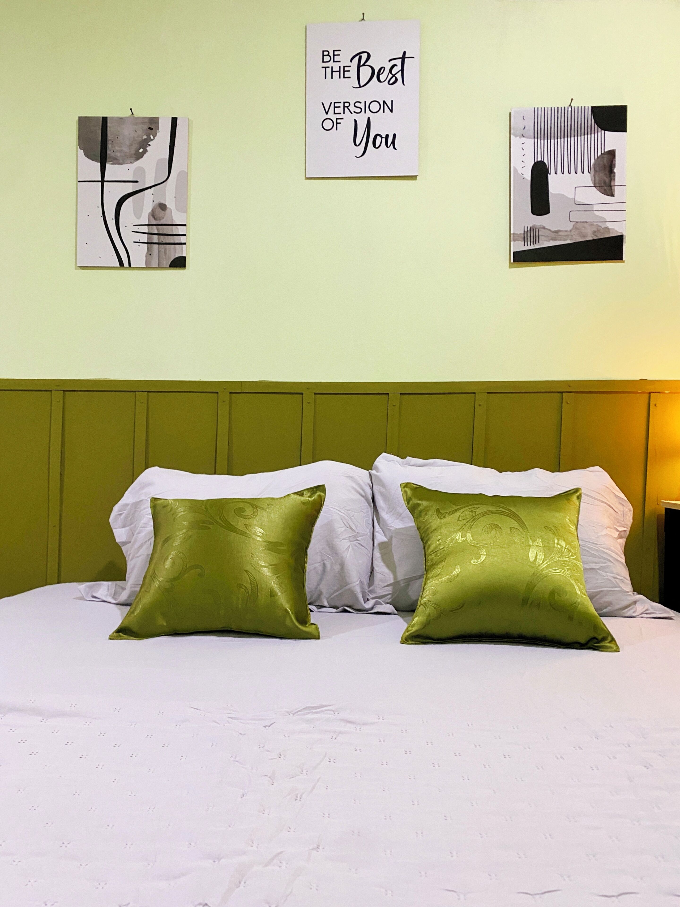 Un lit avec une literie blanche et deux oreillers verts, une tête de lit verte et trois tableaux encadrés accrochés au mur.