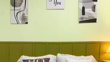 A bed with two pillows, one reading "HOME" and the other "family is everything," against a light green wall with two framed pictures.