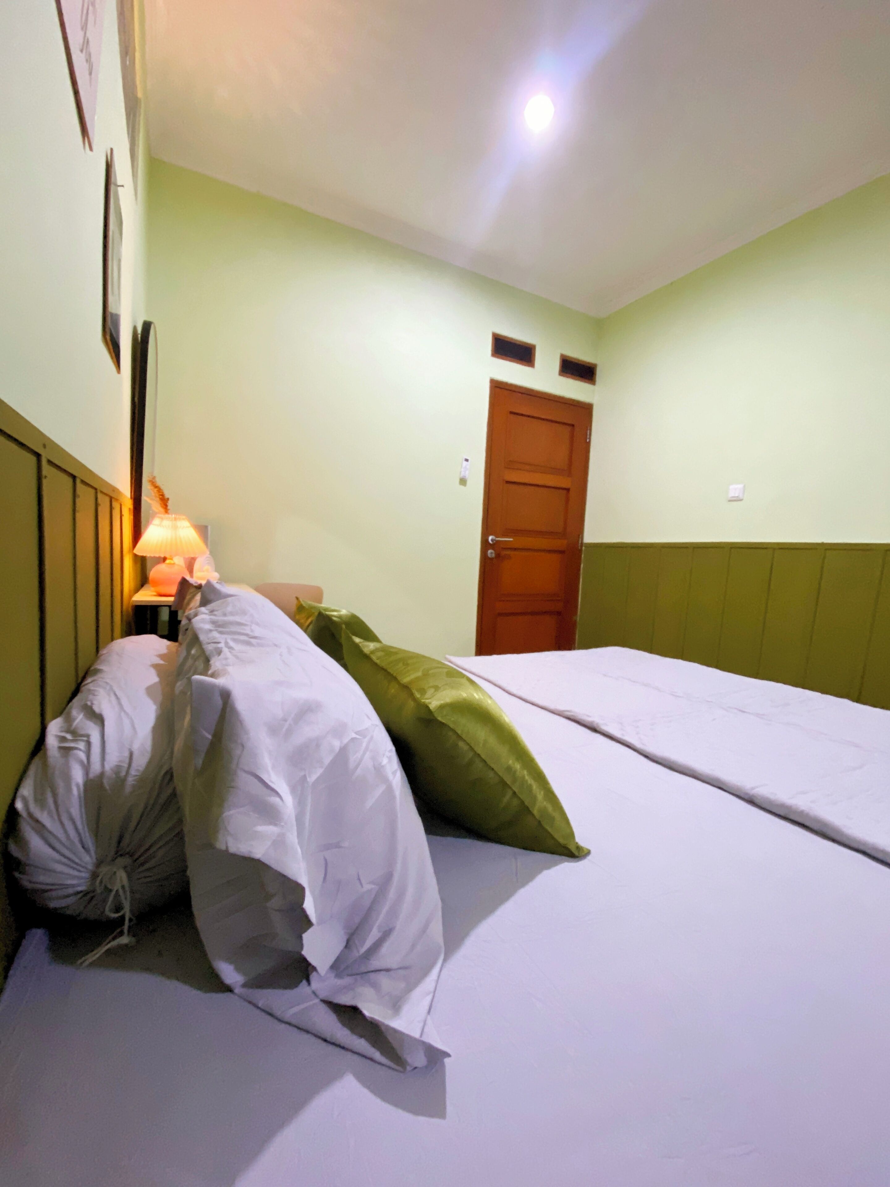 Una cama individual con ropa blanca y almohadas verdes en una habitación con paredes verde claro y una puerta de madera.