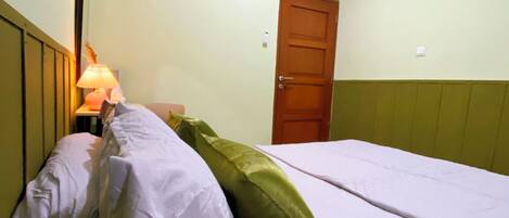 Una cama individual con ropa blanca y almohadas verdes en una habitación con paredes verde claro y una puerta de madera.