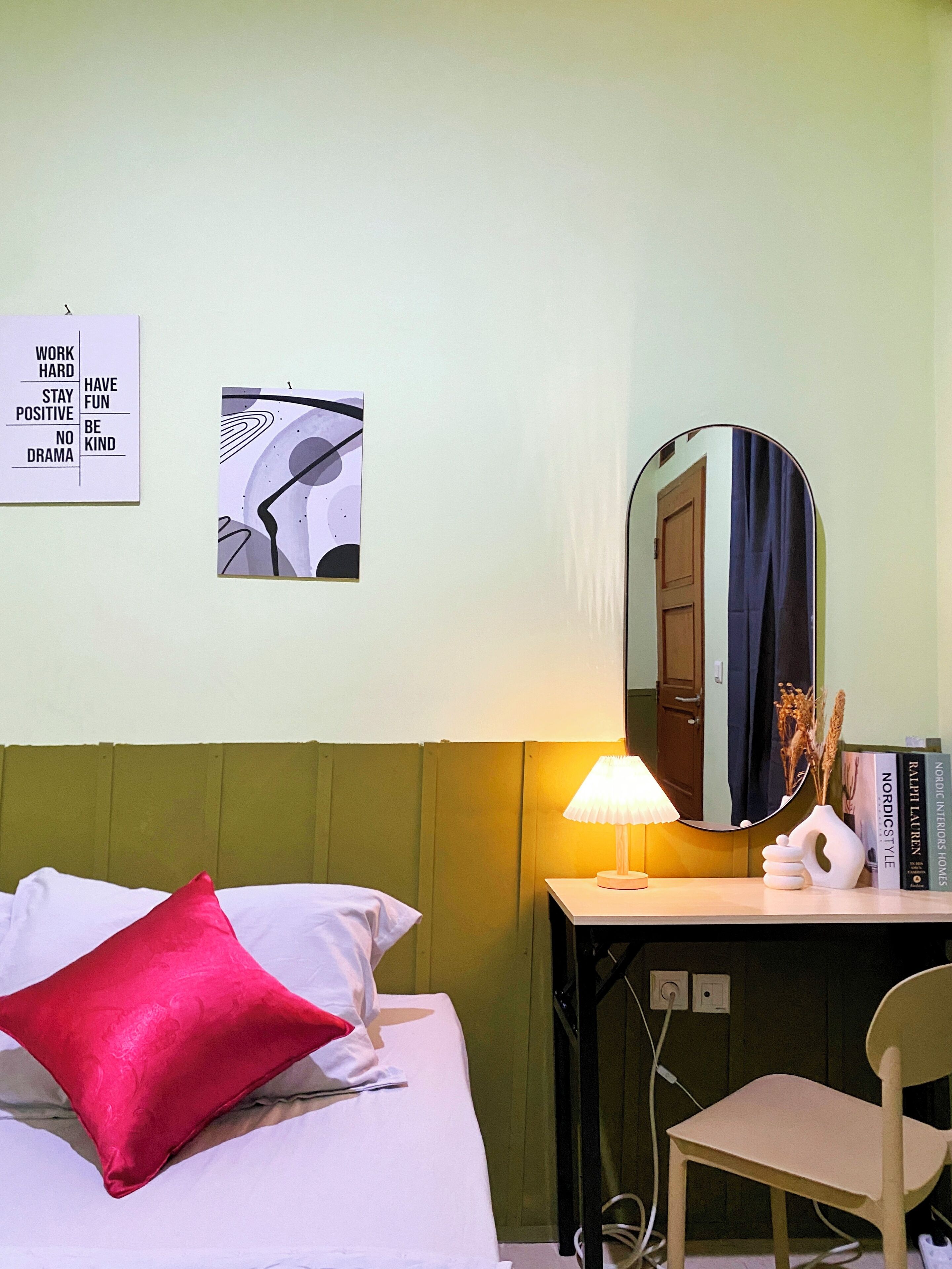 Habitación de hotel con cama, escritorio, silla, lámpara, espejo y dos adornos en la pared.