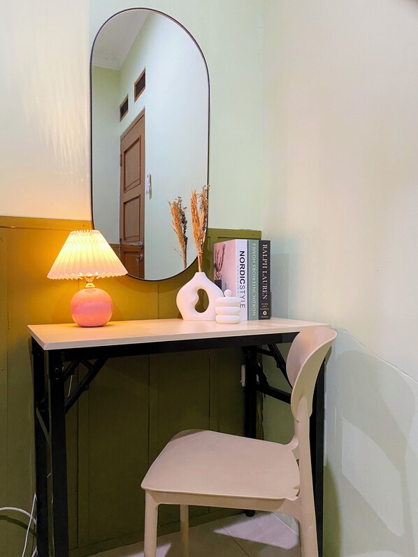 A small desk with a lamp, a mirror, and a few books.