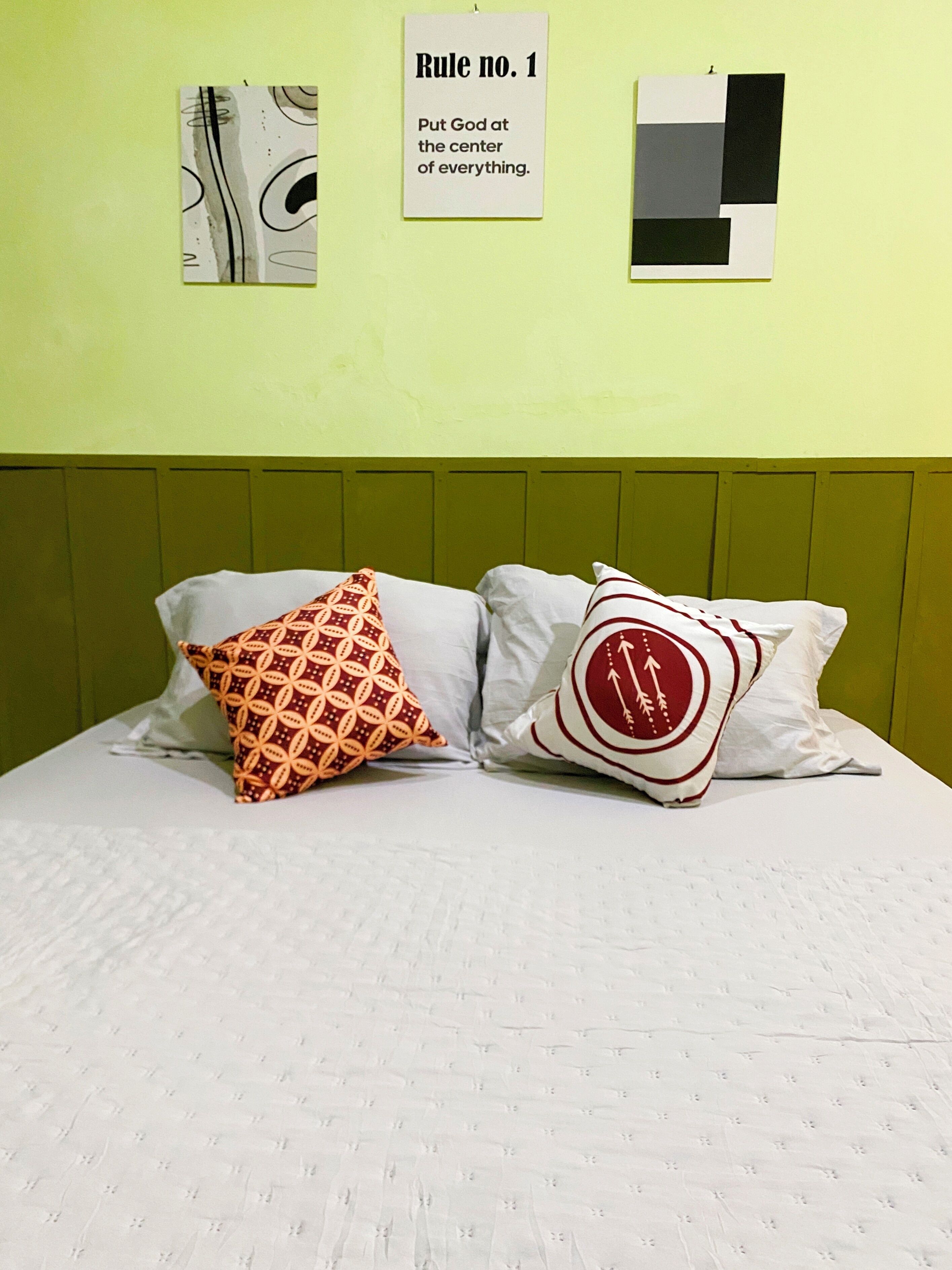 A bed with two patterned pillows and a wall with three framed items, including a sign with text.