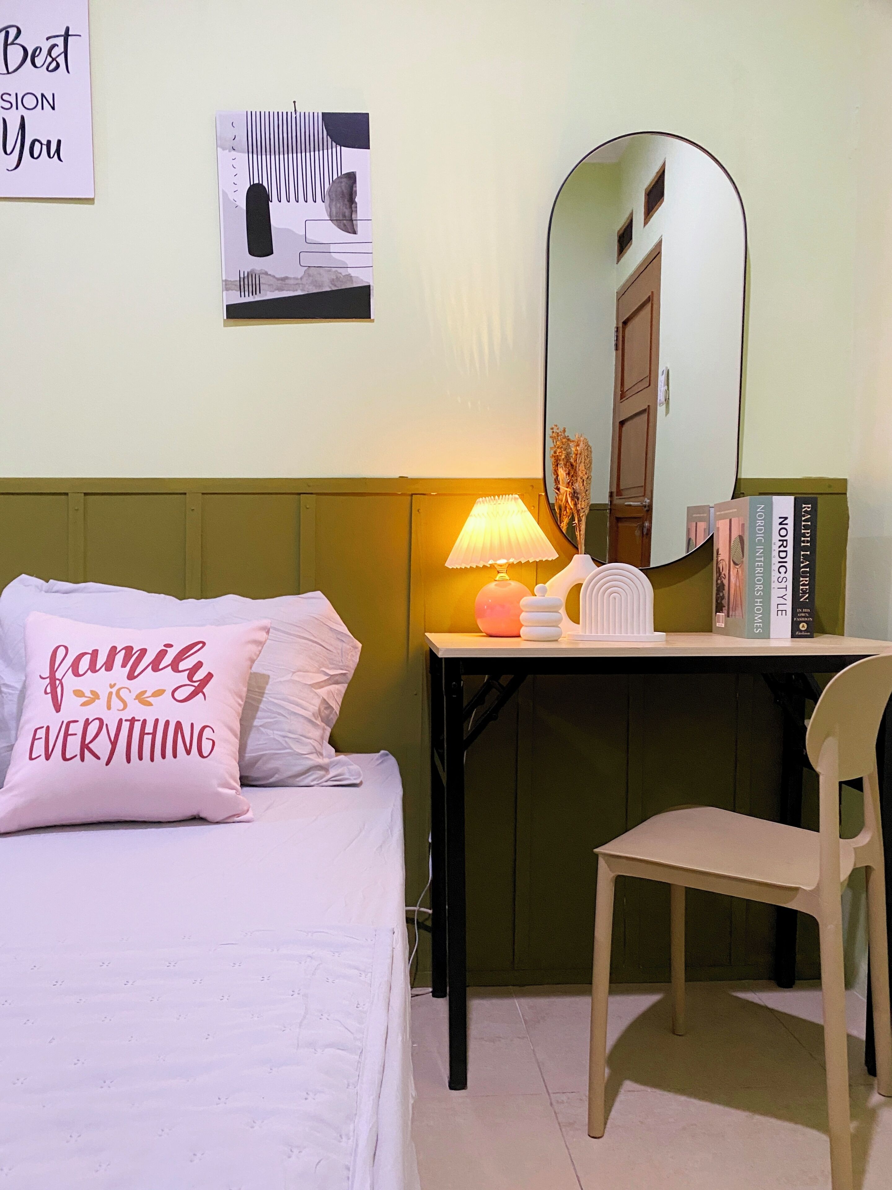 Un dormitorio ordenado con cama, escritorio, silla, lámpara, espejo y algunos libros.