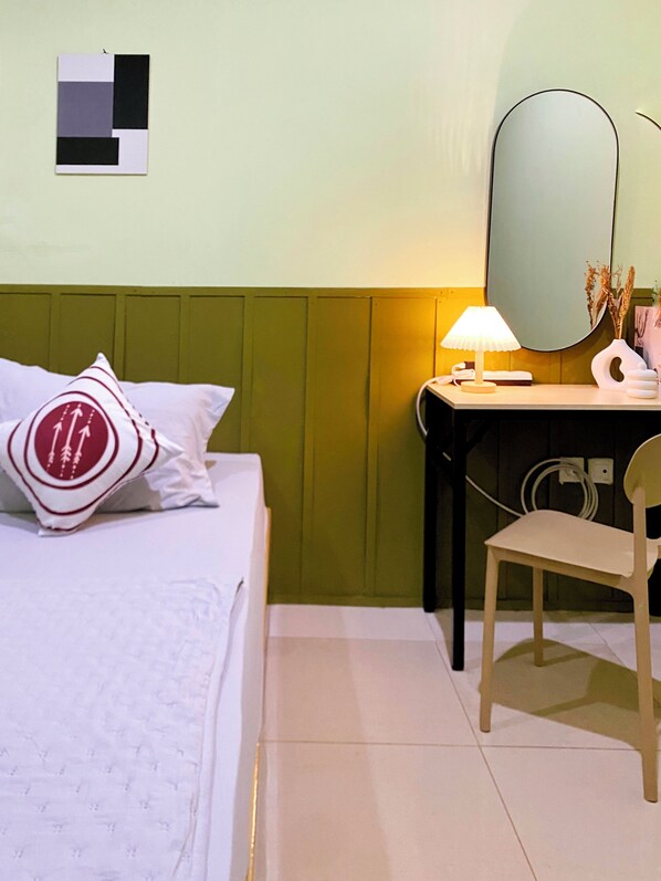 A hotel room with a bed, a desk with a lamp, a chair, and a mirror. - Bandung Co Stay (Bandung)