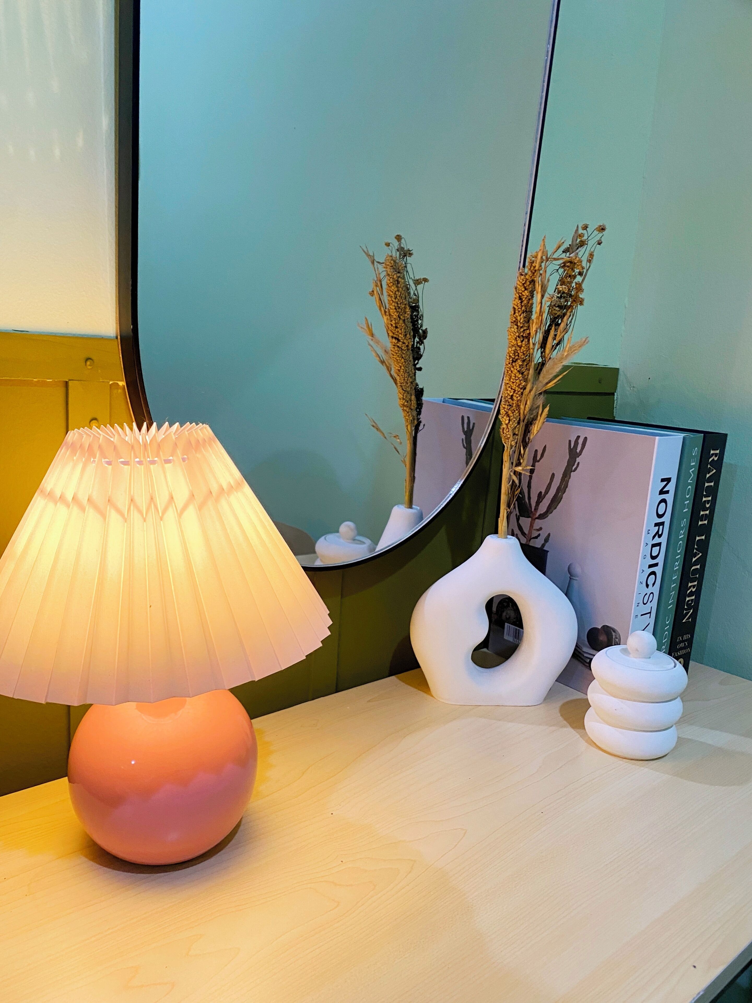 Une table avec une lampe, un vase contenant des plantes séchées et une pile de livres.