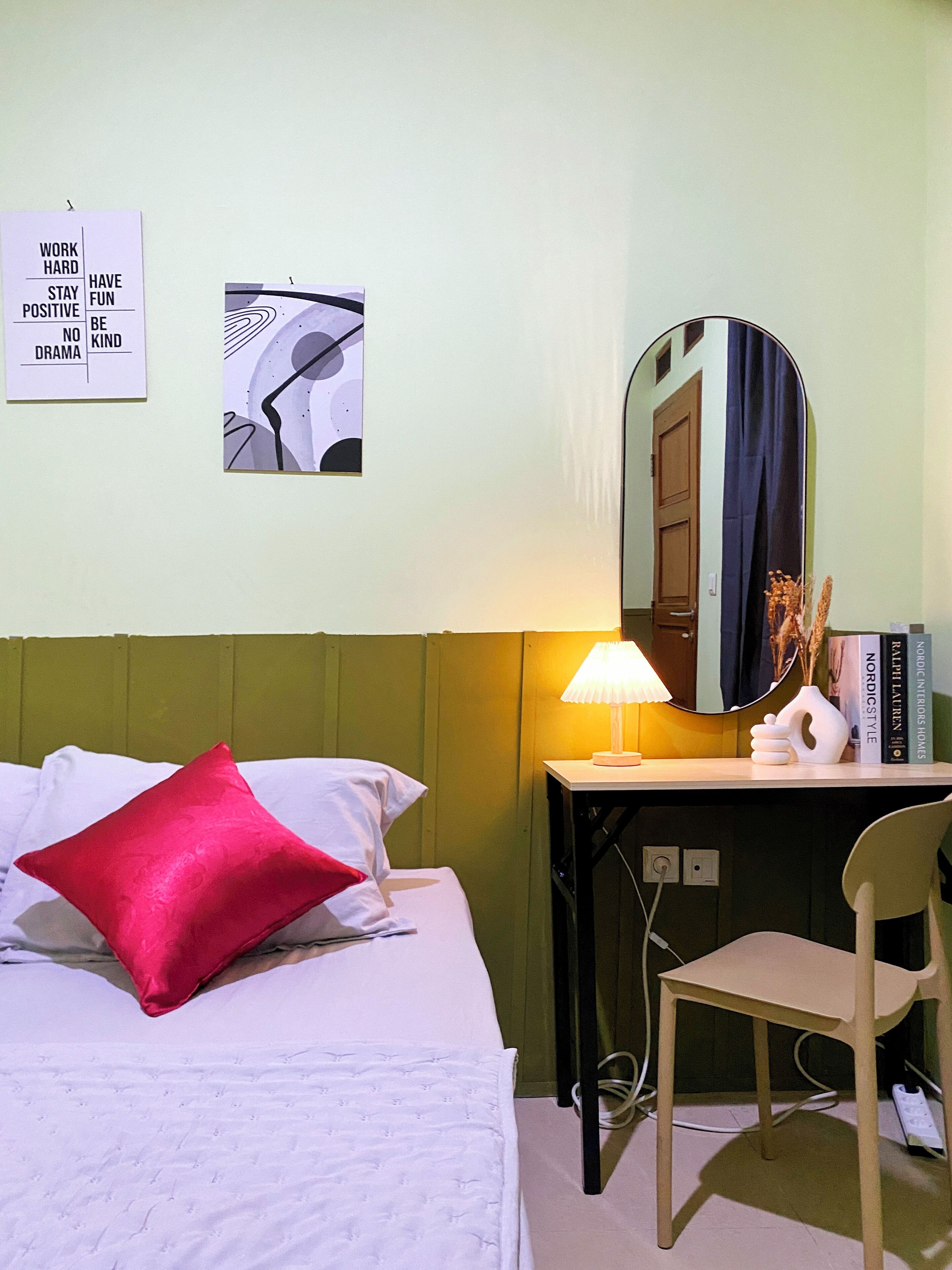 Een hotelkamer met een bed, een bureau, een stoel, een lamp, een spiegel en twee motiverende posters aan de muur.