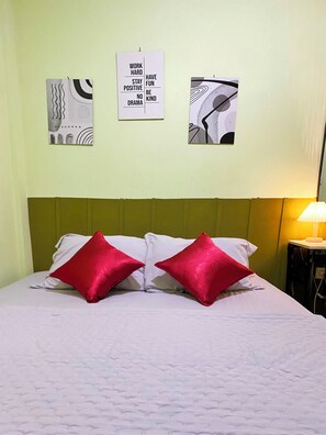 Camera d'albergo con un letto, due cuscini rossi, una testiera verde e tre opere d'arte alle pareti con citazioni motivazionali.
