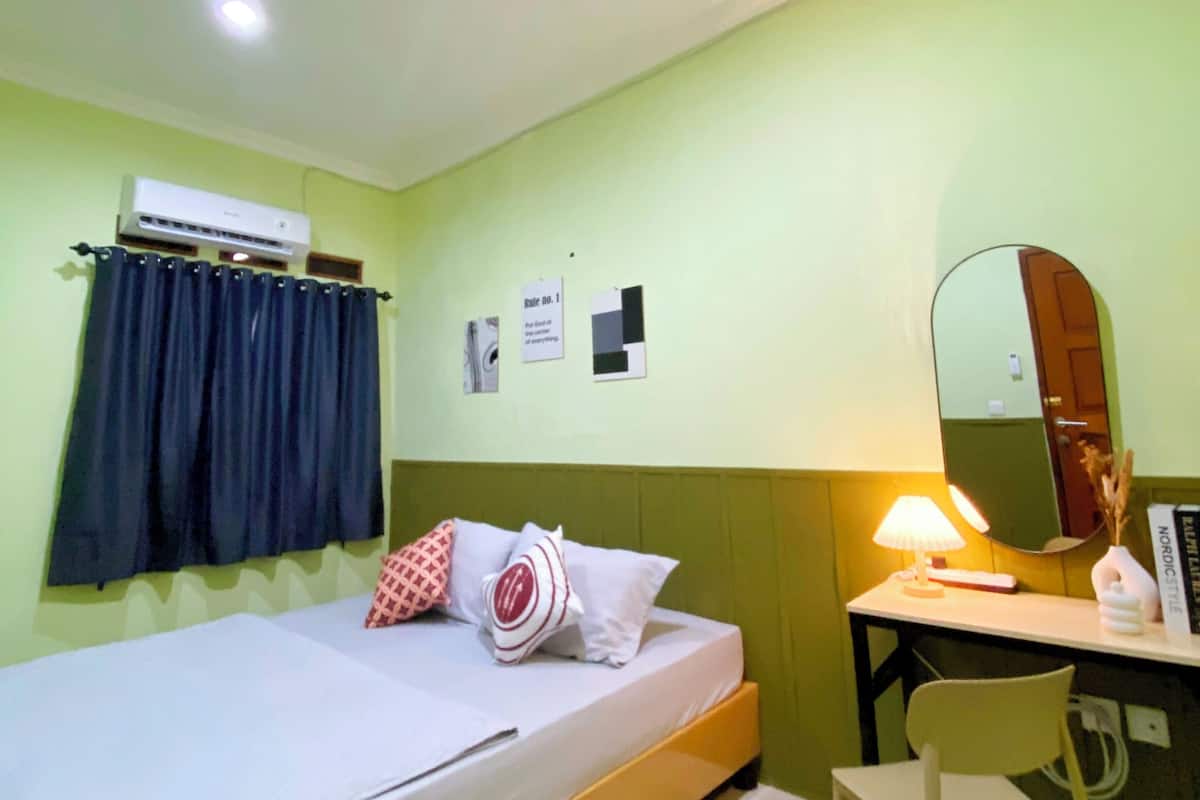 A room with a bed, a desk, a chair, a mirror, and an air conditioning unit.