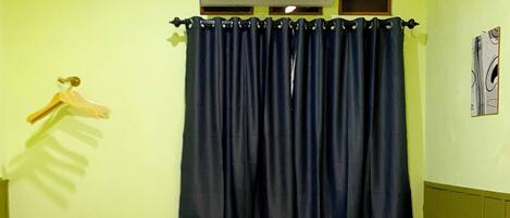 Een hotelkamer met een bed, een hangende airconditioning, een donker gordijn en een aan de muur hangend schilderij.