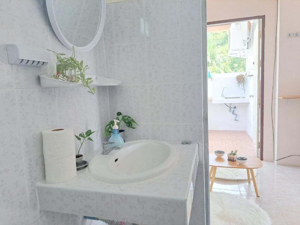 A bathroom with a white sink, a mirror, and a toilet paper roll. There is a small table with a bowl and a plant.