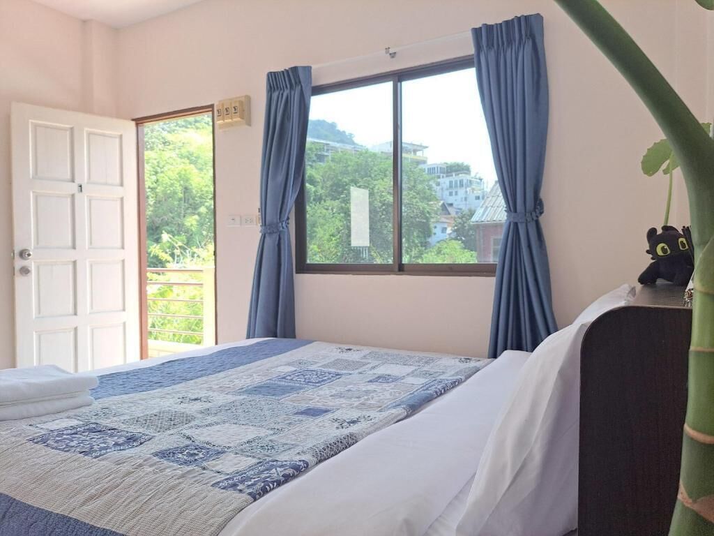 A bedroom with a bed, a window with curtains, a door, and a small plant on a nightstand.