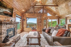 Ein Holzblockhaus-Interieur mit Kamin, einer Couch, einem Essbereich und Blick ins Freie.
