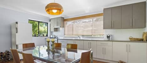Een moderne keuken met een glazen eettafel, houten stoelen en een groot raam.