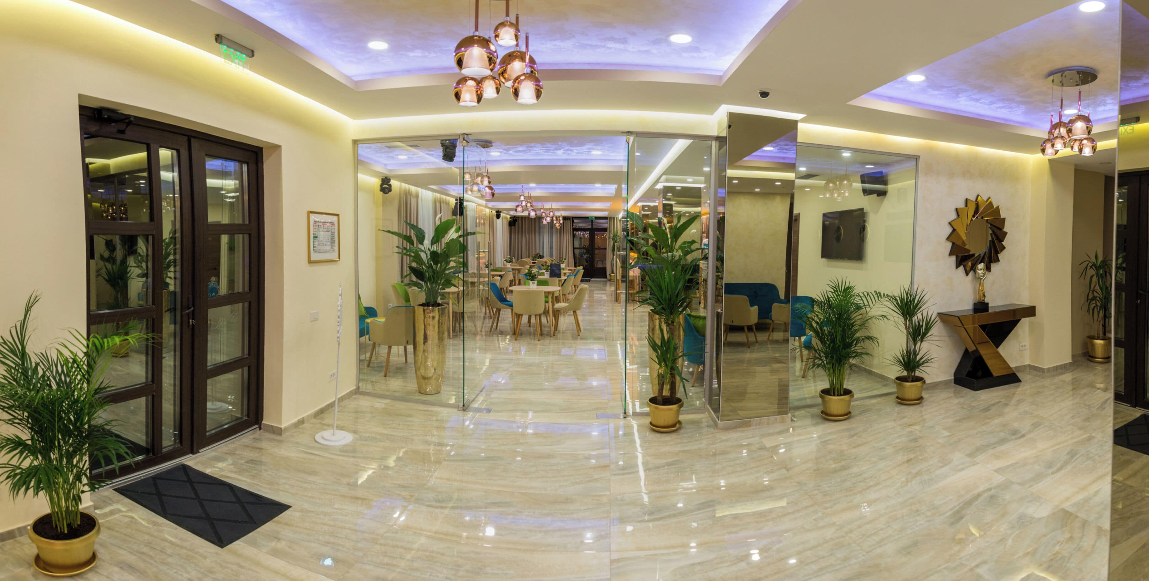 A spacious lobby with a polished marble floor, modern lighting fixtures, and several potted plants.