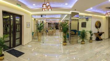 A spacious lobby with a polished marble floor, modern lighting fixtures, and several potted plants.