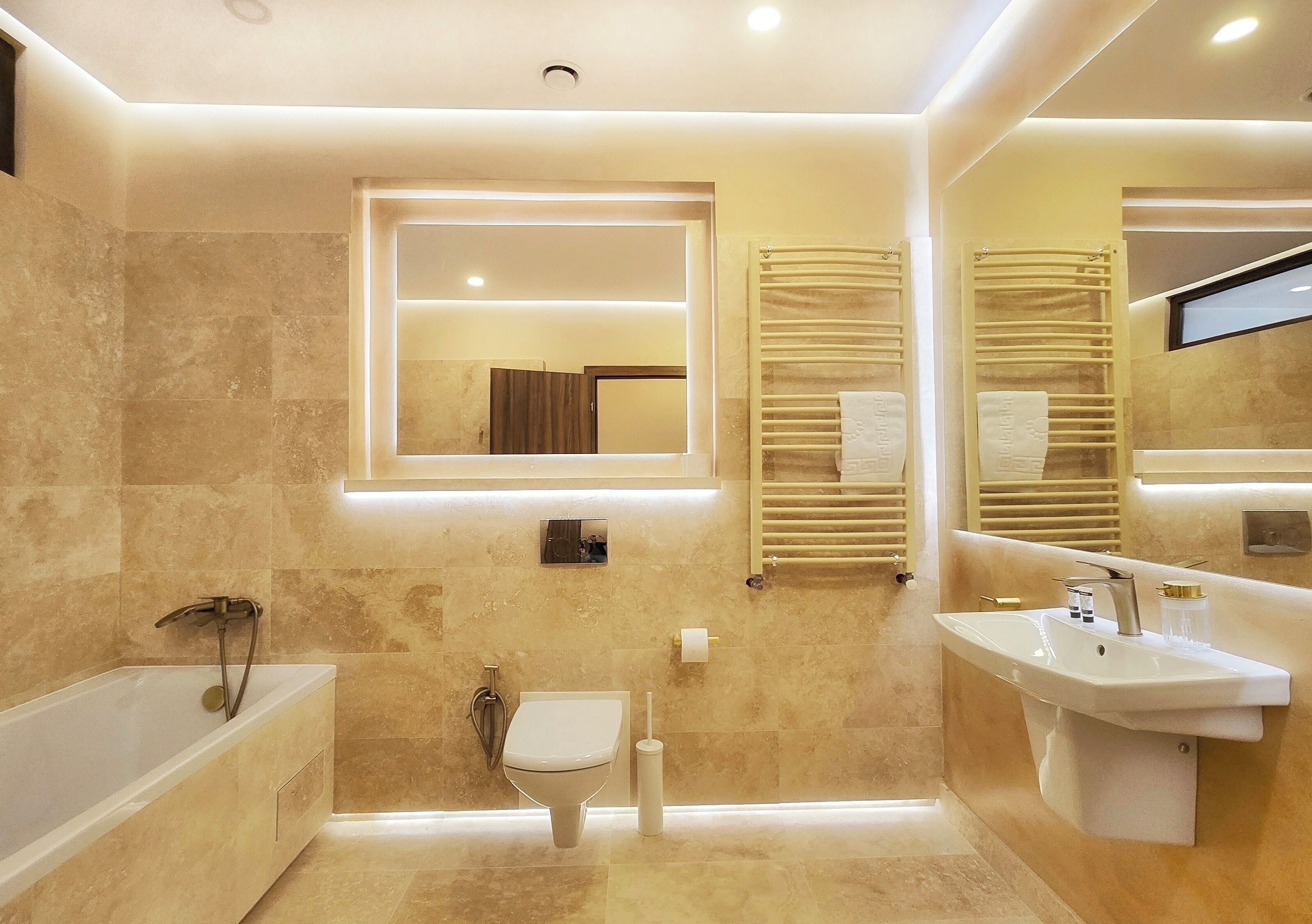Un baño moderno con bañera, inodoro y lavamanos, con azulejos de mármol e iluminación empotrada.