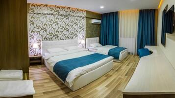 Habitación de hotel con dos camas, suelo de madera, pared con estampado, televisión y ventana con cortinas.