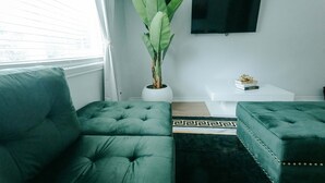 Ein modernes Wohnzimmer mit einem grünen Sofa, einem Blumentopf, einem Couchtisch und einem flachbildfernseher an der Wand.