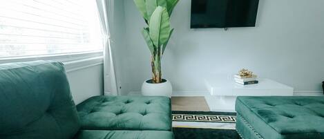 Una sala de estar moderna con un sofá verde, una planta en maceta, una mesa de centro y un televisor de pantalla plana montado en la pared.