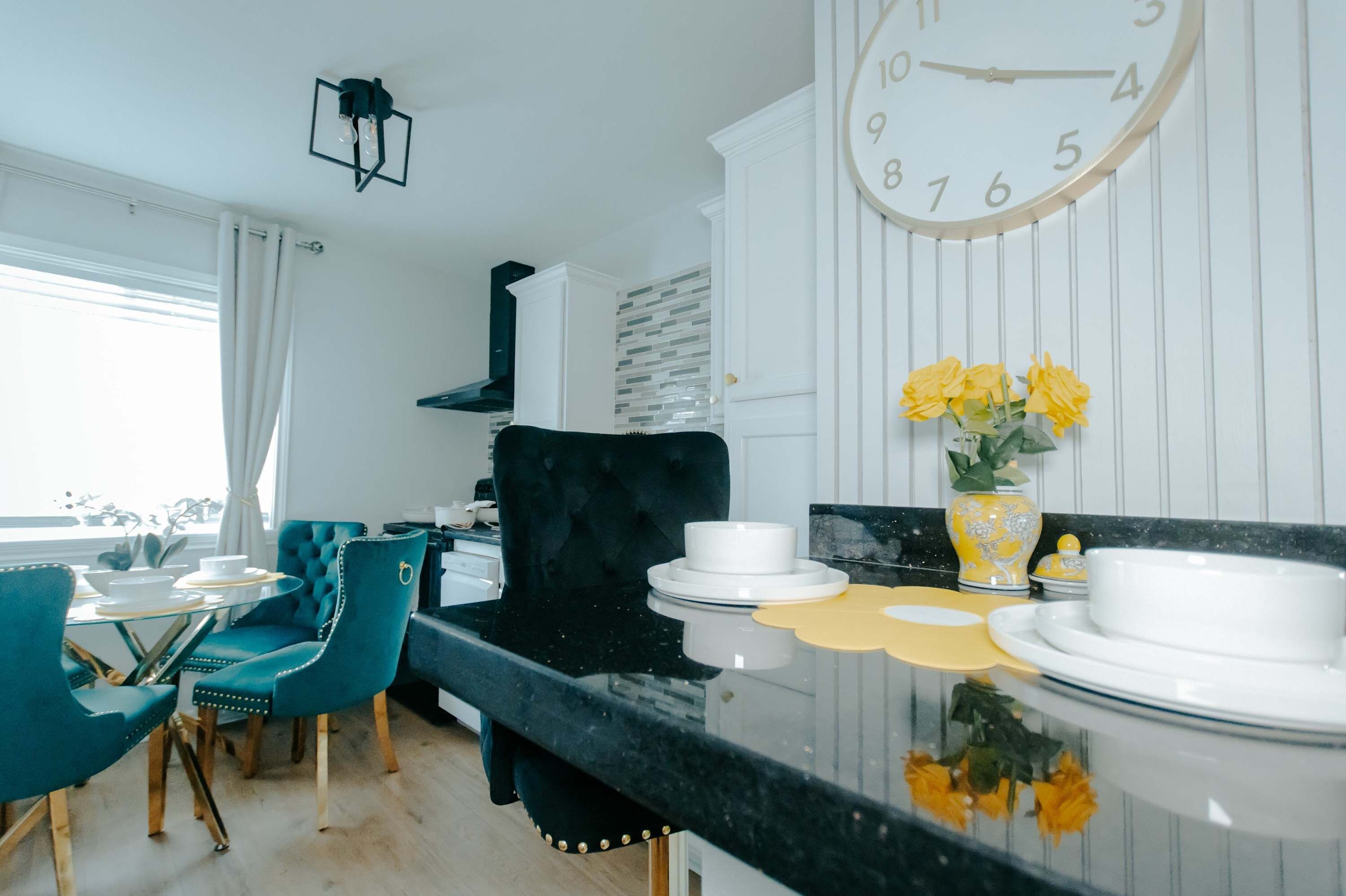 A modern kitchen with a black countertop, white cabinets, and a large wall clock.