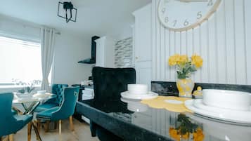 A modern kitchen with a black countertop, white cabinets, and a large wall clock.