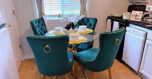 Un espace repas avec une table en verre entourée de chaises recouvertes d’un tissu turquoise et agrémentées d’anneaux dorés.