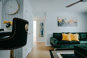 Ein modernes Wohnzimmer mit einem dunkelgrünen Sofa, gelben Kissen, einer Uhr an der Wand und einem Gemälde.