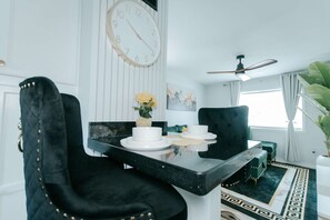 A dining area with a table set for two, a clock on the wall, and a ceiling fan. - Extended-Stay 2BR · Monthly Rates · Near SFA (Nacogdoches)