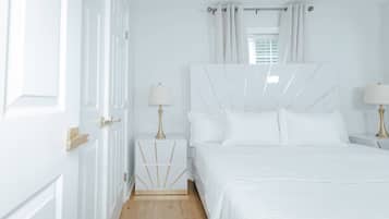 A white bedroom with a bed, bedside tables, and a window with curtains.