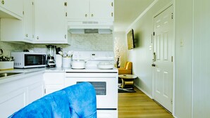 A kitchen with white cabinets, a microwave, a stove, and a dining area with a chair and table. - Sunlit 2BR · Full Kitchen · 2 Min to SFA (Nacogdoches)
