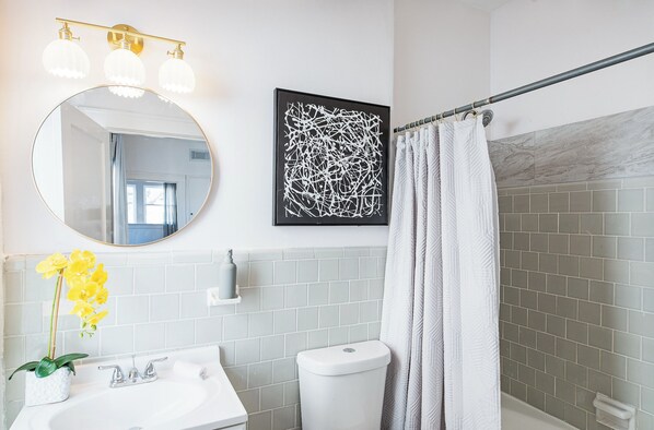 A bathroom with a round mirror, a sink, a toilet, and a shower curtain. - 1BR The Montrose W Main 07, Downtown, Med Center (Houston)
