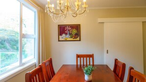 A dining room with a wooden table, six chairs, a chandelier, a painting, and a window with curtains. - Skyline Sanctuary: Green View, Bird Songs, Parking, Espresso & Netflix (Wellington)