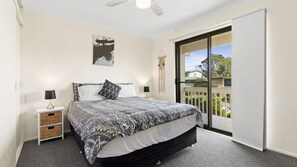 A bedroom with a bed, bedside tables, a ceiling fan, a large window, and a view of the outdoors. - Manyana Deck Life is a spacious pet friendly home (Manyana)