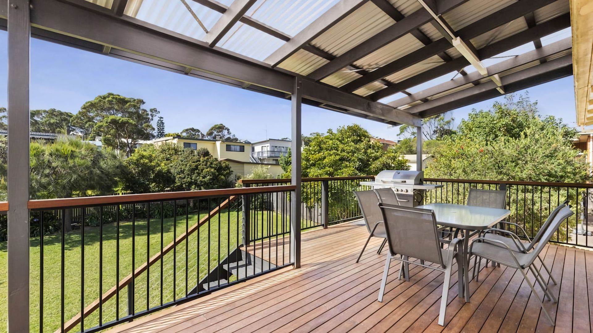 A covered outdoor area with a grill, seating, and a view of the surrounding neighborhood.
