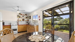 A modern kitchen with wooden cabinets, a white stove, and a dining area with a glass table and wicker chairs. - Manyana Deck Life is a spacious pet friendly home (Manyana)