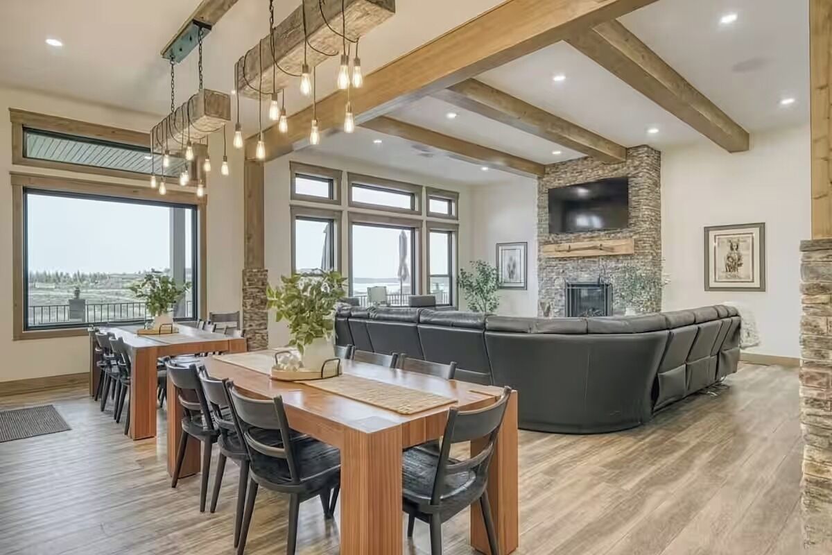 Un amplio salón con un sofá seccional grande, una zona de comedor con una mesa y sillas de madera, y una chimenea de piedra.