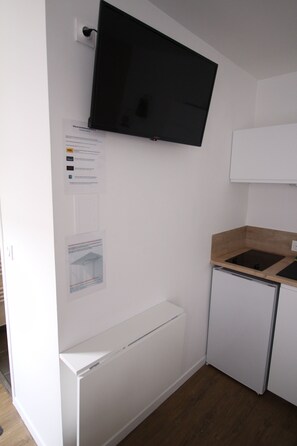 A compact kitchen with a built-in microwave, a small refrigerator, and a flat-screen TV mounted on the wall. - Studio in the very heart of the city, near the Cathedral/Forum/Erlon area (Reims)