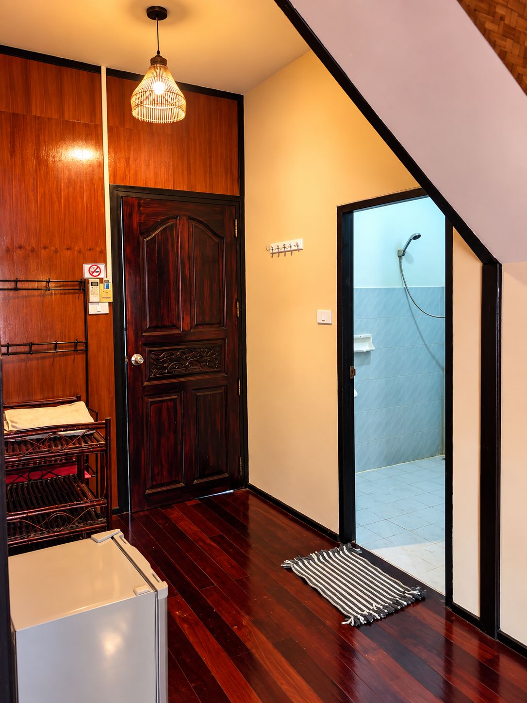 A wooden interior with a door, a hanging light fixture, a coat rack, and a shower area.