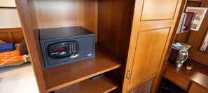 A compact, dark-colored radio with a digital display and keypad, placed on a wooden shelf in a room with a wooden cabinet and a small table with a kettle and a cup. - Marissa Hotel (Ko Pha-ngan)