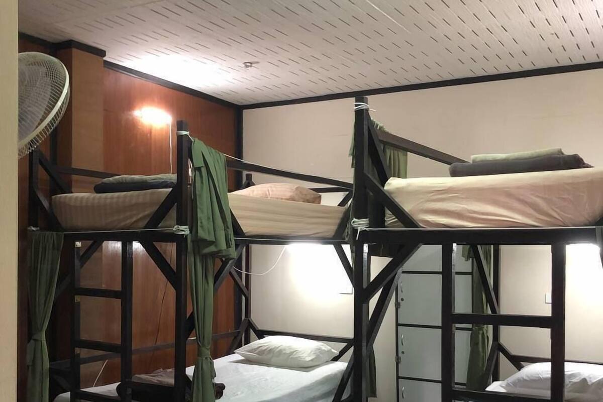 Bunk beds with wooden frames and white bedding, a standing fan, and a wooden floor.