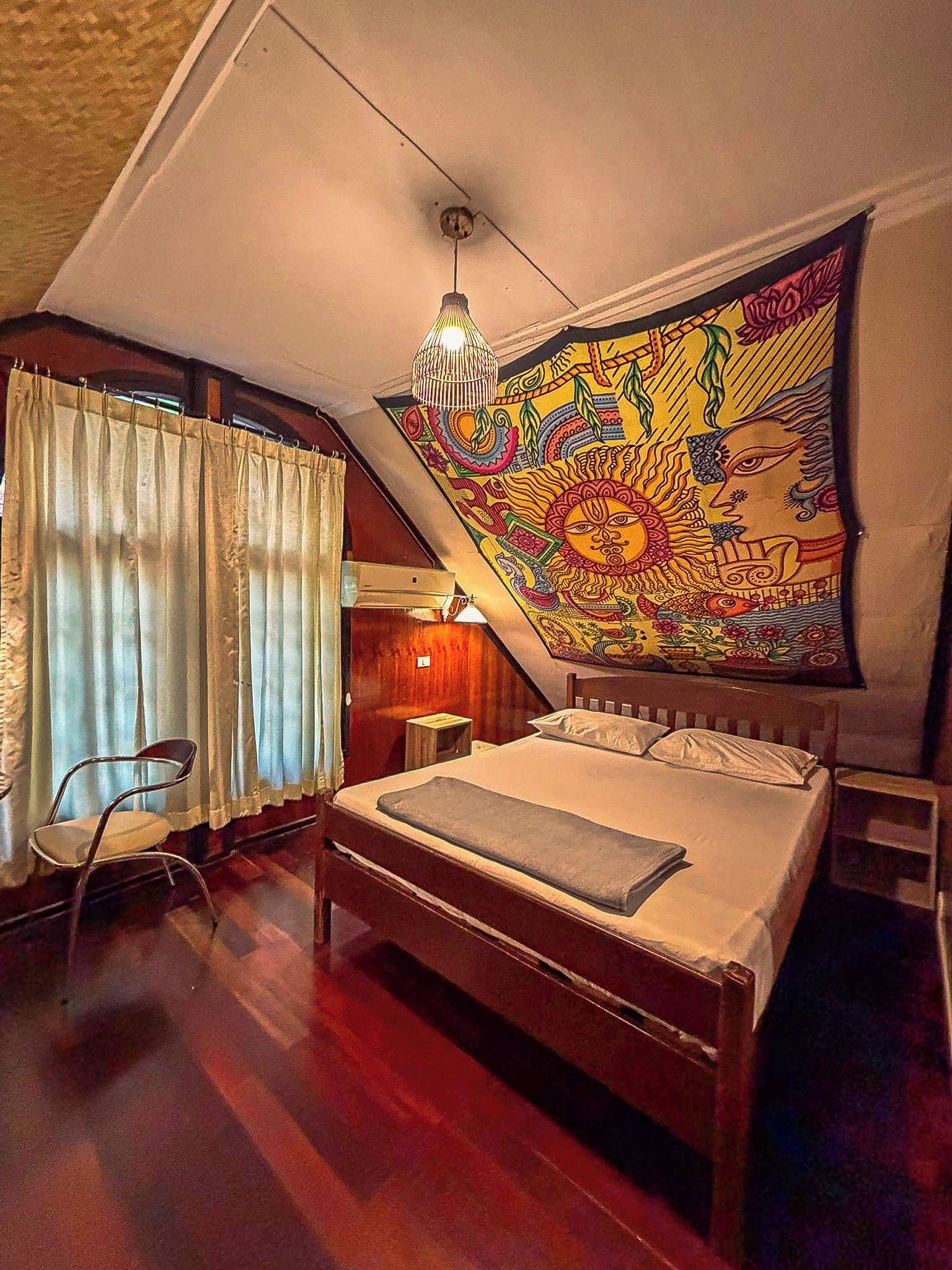 Quarto com cama, cadeira, tapeçaria e luminária pendente.