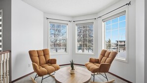 Une pièce d’angle avec deux fauteuils à bascule, une table ronde en bois et trois fenêtres.