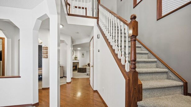 Un couloir avec un escalier en bois, des marches recouvertes de moquette et une porte blanche au fond.