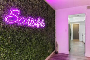 A wall with a neon sign spelling 'Scottsdale' and a hallway leading to a door. - Scottsdale Pool Home, Putting Green, Giant Chess & Shuffleboard Walk to Coffee (Scottsdale)